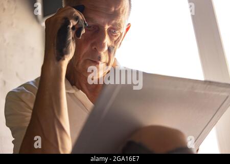 Peintre ou artiste mature ou senior avec crayon graphite devant l'appareil photo. Homme dans une chemise colorée à la peinture travaillant au studio Banque D'Images