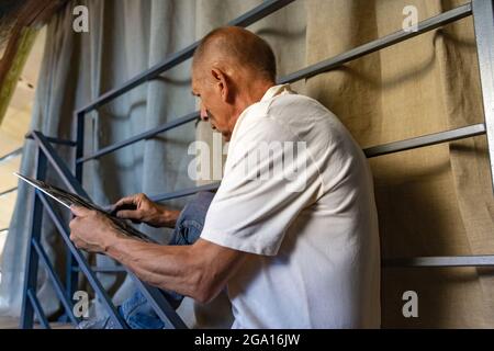 Peintre ou artiste mature ou senior avec crayon graphite devant l'appareil photo. Homme dans une chemise colorée à la peinture travaillant au studio Banque D'Images