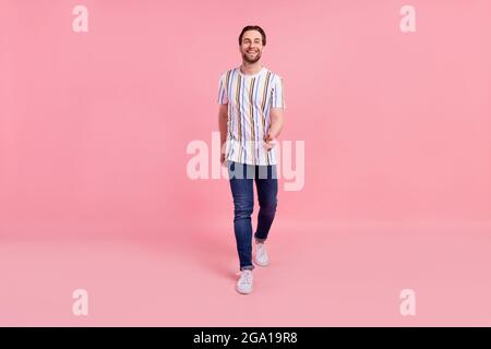 Pleine longueur de corps photo de marche homme dans des vêtements décontractés souriant isolé pastel couleur rose fond Banque D'Images