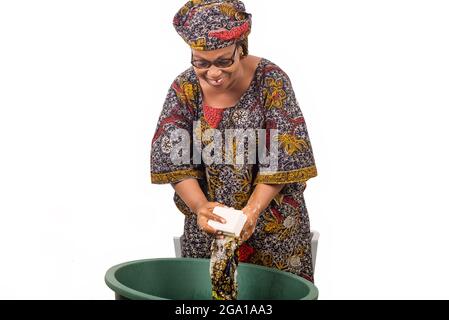 Une femme africaine se tenant au-dessus de la cuve lave les vêtements avec un gros morceau de savon blanc isolé sur fond blanc. Banque D'Images