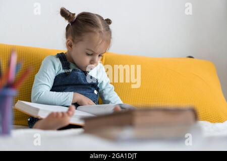 Deux enfants avant-garçonnets lisent un grand livre intéressant de contes de fées sur un lit jaune. Frères et sœurs petits jumeaux lecteur ont plaisir, heureux enfant sur Banque D'Images