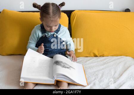 Deux enfants avant-garçonnets lisent un grand livre intéressant de contes de fées sur un lit jaune. Frères et sœurs petits jumeaux lecteur ont plaisir, heureux enfant sur Banque D'Images