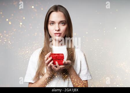Une jeune femme souriante tient une boîte-cadeau fermée avec des bijoux, autour de la paillette. Le concept de vacances, cadeaux. Photo de haute qualité Banque D'Images
