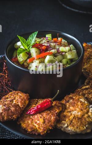 Salade de concombre frais dans un bol noir avec des viandes de poisson ou de légumes ou des boulettes de viande autour, verticalement Banque D'Images