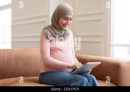 Vue latérale d'une femme musulmane enceinte utilisant une tablette à la maison Banque D'Images
