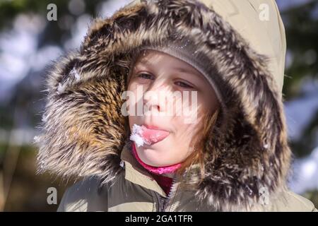 Une petite fille attrapant des flocons de neige sur la langue. Un enfant heureux qui marche à l'extérieur par temps froid et ensoleillé et qui profite de l'hiver. Banque D'Images