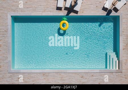 Piscine vide rectangulaire bleue avec chaises longues et parasols et grand tube flottant jaune ananas gonflable. Louez un bien immobilier ou faites une somme Banque D'Images