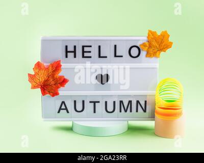Texte Hello Autumn sur la visionneuse avec les feuilles d'automne sur le podium vert Banque D'Images