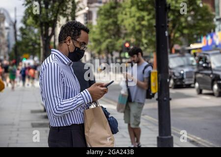Des hommes utilisant leur smartphone lors de leurs déplacements sur Oxford Street, Central London, Angleterre, Royaume-Uni Banque D'Images