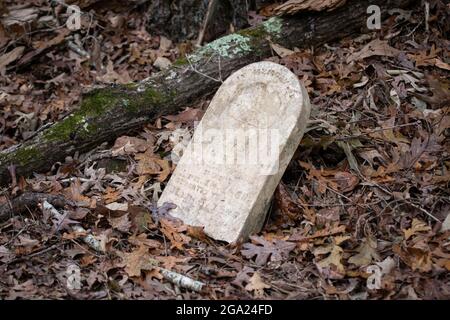 Ancienne pierre à tête du XIXe siècle portée avec le temps dans un vieux cimetière surcultivé dans les bois de l'Alabama rural. Banque D'Images