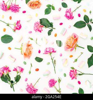 Motif avec fleurs roses et feuilles avec bonbons sur fond blanc. Flat lay, vue de dessus. Banque D'Images