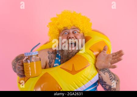 FAT Happy man avec perruque dans la tête est prêt à nager avec un donut sauvetage Banque D'Images