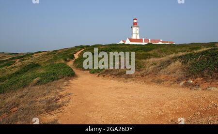 Sentier de terre qui monte sur la colline verte jusqu'au phare blanc, cap Espichel, Portugal Banque D'Images