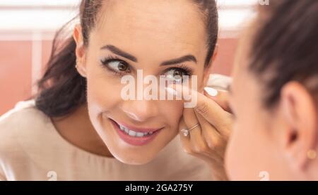 Une jeune femme met des lentilles de contact dans les yeux le matin dans la salle de bains, devant un miroir. Banque D'Images