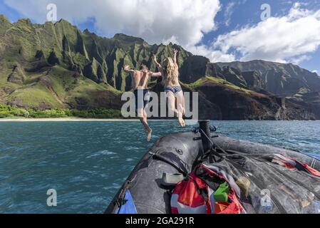 Un jeune homme et une jeune femme sautent d'un bateau gonflable dans l'eau de l'océan au large de la côte sauvage de Napali de Kauai Banque D'Images