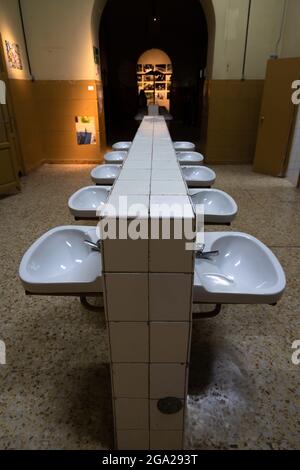 Toilettes publiques à faible éclairage dans lesquelles vous pouvez voir une double rangée de lavabos reliés par un mur de carrelage blanc, avec l'arrière-plan éclairé et hors de foc Banque D'Images