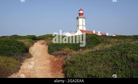Sentier de terre qui monte sur la colline verte jusqu'au phare blanc, cap Espichel, Portugal Banque D'Images