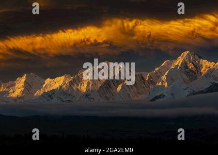Des nuages spectaculaires et une chaîne de montagne enneigée en hiver au lever du soleil avec une lumière chaude et des points forts sur les nuages et les montagnes avec du brouillard dans le val... Banque D'Images