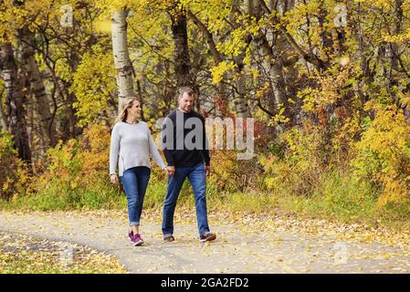 Un couple mature et marié passe du temps ensemble dans un parc de la ville pendant la saison d'automne, en marchant sur un sentier et en tenant les mains Banque D'Images