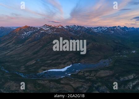 Vue aérienne des spectaculaires chaînes de montagnes et d'une rivière traversant la toundra le long de l'autoroute Dempster au coucher du soleil; Yukon, Canada Banque D'Images