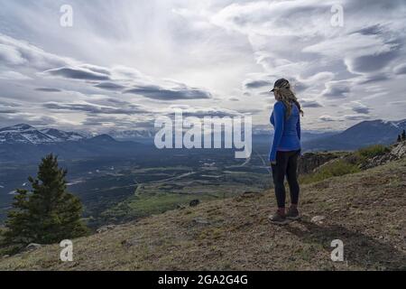 Vue de l'arrière d'une femme qui se tient sur un sommet de montagne et qui donne sur la vue des majestueuses chaînes de montagnes et de la vallée en dessous avec un... Banque D'Images