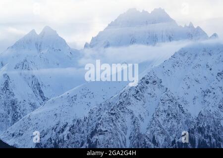 Gros plan sur les sommets enneigés majestueux des montagnes avec des nuages brumeux dans la lumière douce du matin; Haines, Alaska, États-Unis d'Amérique Banque D'Images