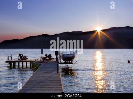 Des chaises Adirondack et une table de pique-nique sont assises sur un quai en bois avec un bateau et un ascenseur sur le lac Okanagan au coucher du soleil; Colombie-Britannique, Canada Banque D'Images