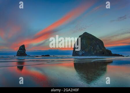 Coucher de soleil spectaculaire dans les nuages au-dessus de la plage et des formations rocheuses sur la côte de l'Oregon; Cannon Beach, Oregon, États-Unis d'Amérique Banque D'Images