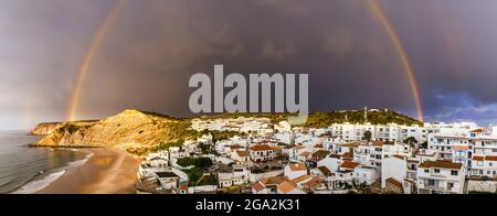 Arc-en-ciel au-dessus du village de pêcheurs traditionnel de Burgau sous un ciel orageux dans la municipalité de Vila do Bispo dans la région occidentale de l'ALG... Banque D'Images