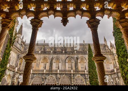 Vue à travers les colonnes ornées du cloître vers le haut aux nuages gris dans la cour intérieure vers la chapelle du monastère médiéval ... Banque D'Images