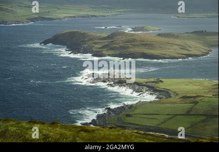 Vue aérienne des vagues se brisant le long de la côte sauvage de Valentia par un jour ensoleillé avec le phare de l'île de Valentia sur Cromwell point, construit sur... Banque D'Images