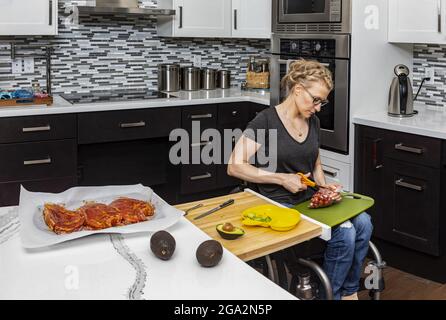 Une femme paraplégique préparant un repas pour sa famille dans sa cuisine tout en travaillant à partir d'un fauteuil roulant; Edmonton, Alberta, Canada Banque D'Images