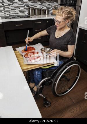 Une femme paraplégique préparant des steaks pour un repas pour sa famille dans sa cuisine tout en travaillant en fauteuil roulant; Edmonton, Alberta, Canada Banque D'Images