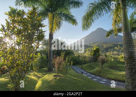 Vue à travers un paysage tropical avec un chemin de pierre vers le soleil levant sur le volcan Arenal; province d'Alajuela, Costa Rica Banque D'Images