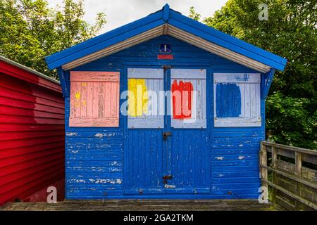 Cabane de plage à Whitstable, Kent, portée par le temps. Bleu avec panneaux carrés peints en bleu clair, rouge, jaune et rose. Banque D'Images