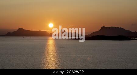 Soleil de minuit illuminant les sommets des montagnes et réfléchissant sur l'océan Atlantique Nord ; Lofoten, cercle arctique, Norvège Banque D'Images