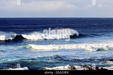 Les vagues éclaboussant créent un arc-en-ciel de couleur dans la brume avec un paysage marin bleu et un ciel nuageux au parc de la plage de Ho'okipa Banque D'Images