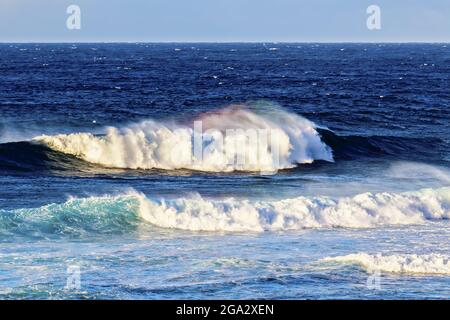 Les vagues éclaboussant créent un arc-en-ciel de couleur dans la brume avec un paysage marin bleu et un ciel nuageux au parc de la plage de Ho'okipa Banque D'Images