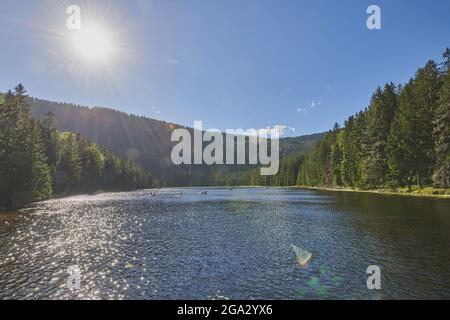 Sunburst au-dessus du lac Arbersee avec des gens dans des bateaux sur l'eau dans le parc national de la forêt bavaroise; Bavière, Allemagne Banque D'Images