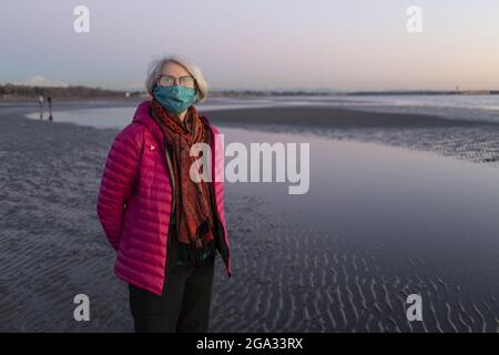 Une femme âgée se tient sur une plage humide portant un masque facial pendant la pandémie mondiale de 2020; White Rock, Colombie-Britannique, Canada Banque D'Images