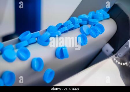 Ligne de production - de nombreux bouchons de bouteilles en plastique bleu tombent du tapis transporteur Banque D'Images