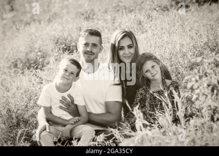 Portrait noir et blanc d'une famille de quatre enfants avec deux jeunes enfants assis sur l'herbe dans un parc; Edmonton, Alberta, Canada Banque D'Images