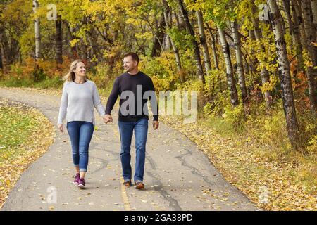Un couple marié mature qui passe du temps ensemble de qualité à marcher à l'extérieur dans un parc de la ville pendant un après-midi d'automne chaud; St. Albert, Alberta, Canada Banque D'Images