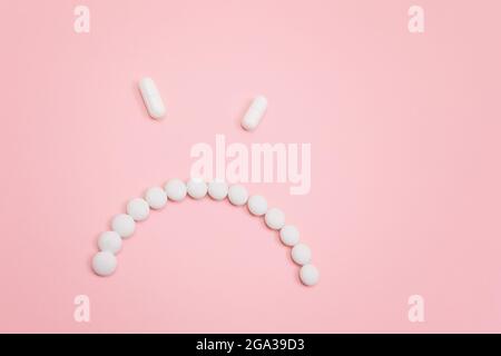 Préjudice pharmaceutique. Angry Smiley visage fait de pilules blanches, couché sur le Backgrond rose. Industrie pharmaceutique mondiale et médicaments Banque D'Images