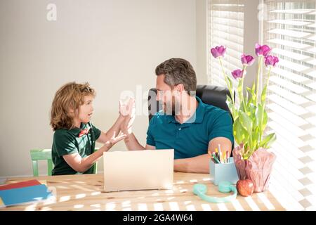 le père et l'enfant fils émerveillés à l'école travaillant en ligne sur ordinateur portable, l'ensemble Banque D'Images