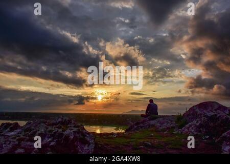 Cachemire, Inde. 28 juillet 2021. Un homme repose sur une colline au coucher du soleil à Manasbal, à environ 30 km de Srinagar. Le Département météorologique de l'Inde a publié mercredi une alerte météorologique pour Jammu-et-Cachemire, prédisant des pluies abondantes qui peuvent causer des inondations soudaines, des glissements de terrain et aussi l'exploitation forestière de l'eau dans les zones de basse altitude. Au moins sept personnes ont été tuées et 19 sont restées disparues après des inondations soudaines qui ont frappé le district montagneux reculé de Jammu & Cachemire, à la suite d'une explosion de nuages mercredi. Crédit : SOPA Images Limited/Alamy Live News Banque D'Images