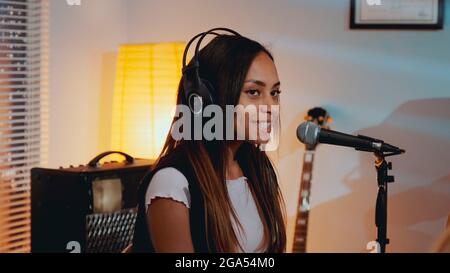 Gros plan sur une belle fille souriante dans un casque chantant sa chanson préférée sur la répétition en studio à la maison le soir. Banque D'Images