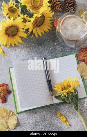 Bonjour. Concept de liste des tâches. Un bouquet de grands tournesols, une tasse de café et un carnet vide sur une table en pierre. Banque D'Images