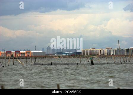 Une vue depuis les eaux côtières de Bekasi juste avant la frontière avec Jakarta, Indonésie. La nouvelle zone commerciale appelée Marunda Makmur sur l'estuaire du canal d'inondation de Jakarta (à gauche) et les nouveaux bâtiments plats dans le village de Marunda à Jakarta (à droite) sont photographiés dans un arrière-plan de certains des bâtiments imposants de la capitale. Banque D'Images