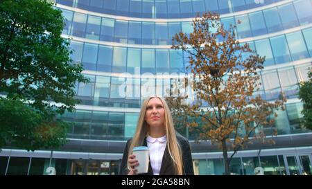 Par en dessous de la blonde woman in suit le café dans la tasse de papier à l'écart sur rue. Banque D'Images